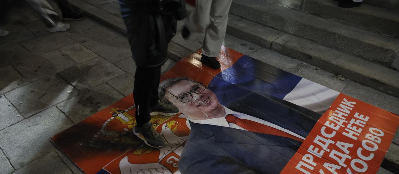 Menschen treten auf ein Plakat auf dem Aleksandar Vucic zu sehen ist.