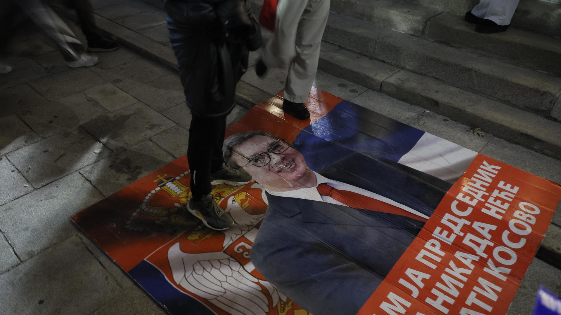 Menschen treten auf ein Plakat auf dem Aleksandar Vucic zu sehen ist. | EPA