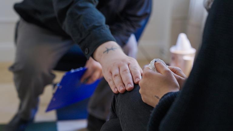 Jemand legt seine Hand auf das Knie einer anderen Person.