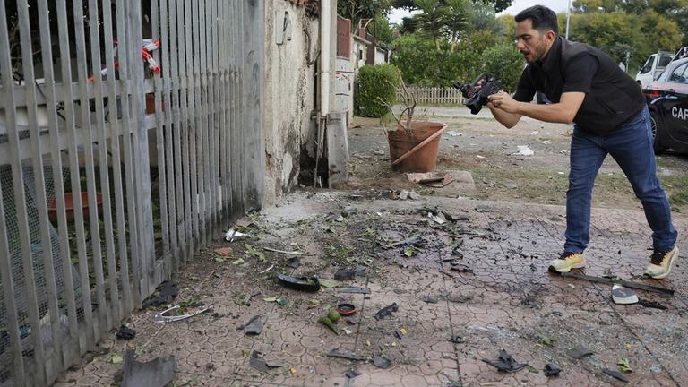 Ein Reporter filmt Teile eines Autos, die auf dem Boden liegen, nachdem unter dem Auto in Pome ein Sprengsatz detoniert ist.