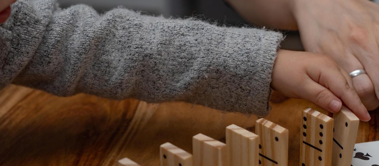 Ein Kind und eine erwachsene Person spielen Domino.