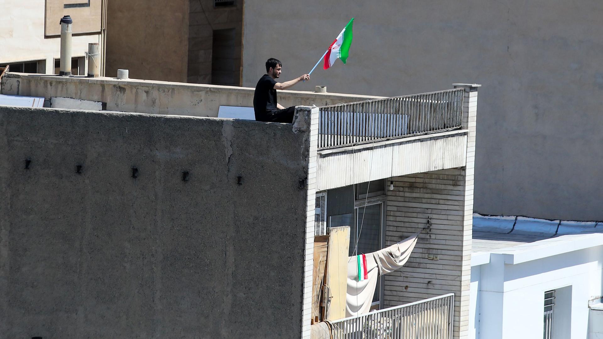 Ein Mann schwenkt die iranische Flagge von der Spitze eines Gebäudes in Teheran.  | Stringer/dpa