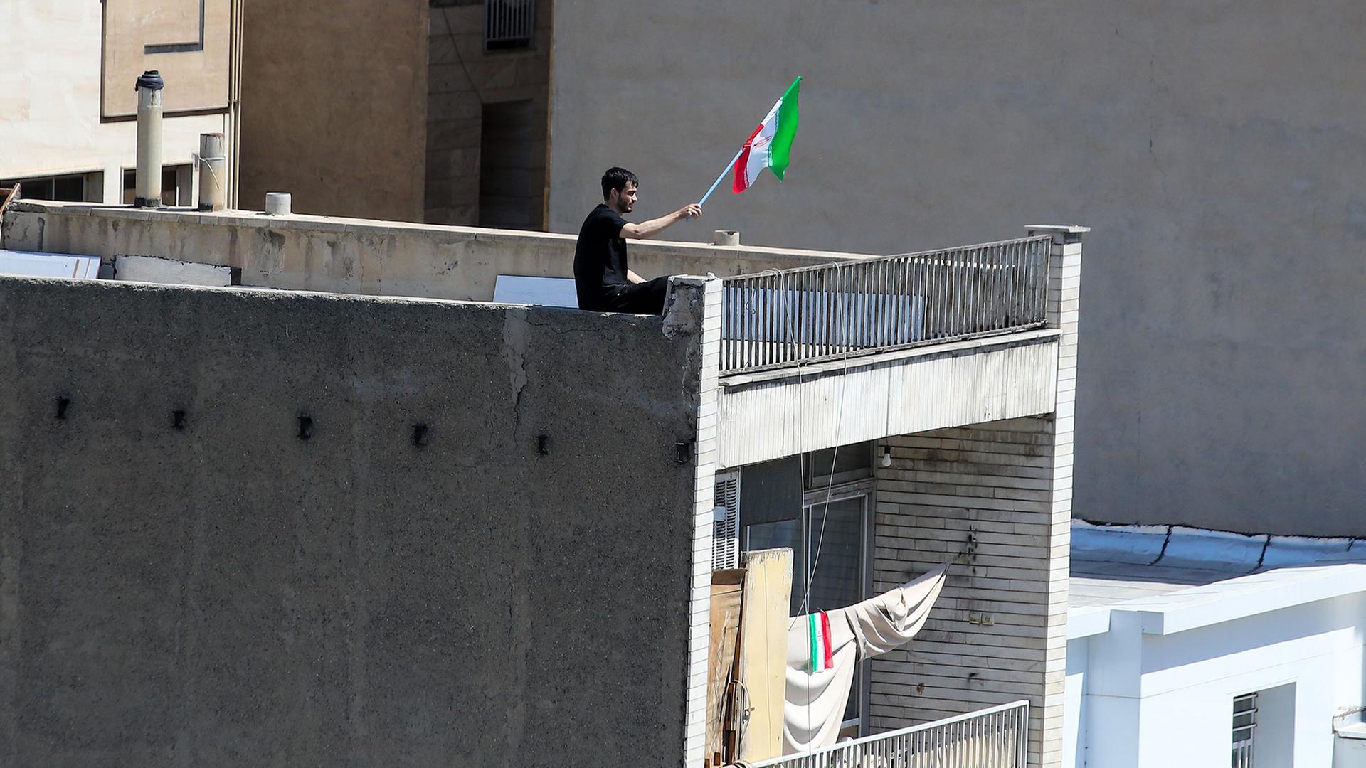 Ein Mann schwenkt die iranische Flagge von der Spitze eines Gebäudes in Teheran.  | Stringer/dpa