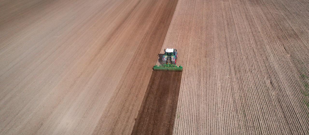 Ein Traktor zieht eine Egge über ein Feld und bereitet den Boden auf die Aussaat vor.