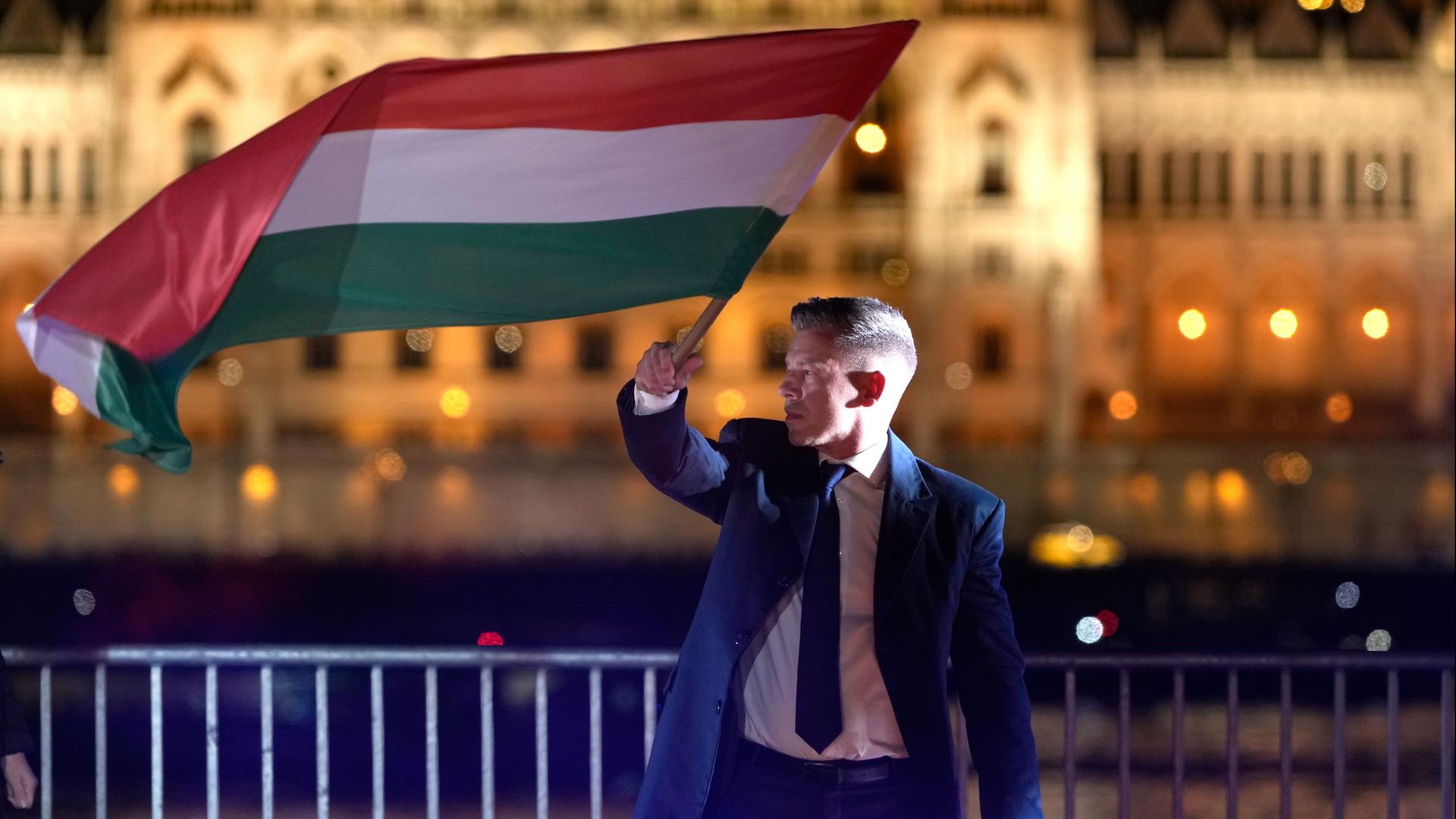 Peter Magyar, der Vorsitzende der Oppositionspartei Tisza, schwenkt nach der Parlamentswahl eine Nationalflagge. | Darko Bandic/AP/dpa