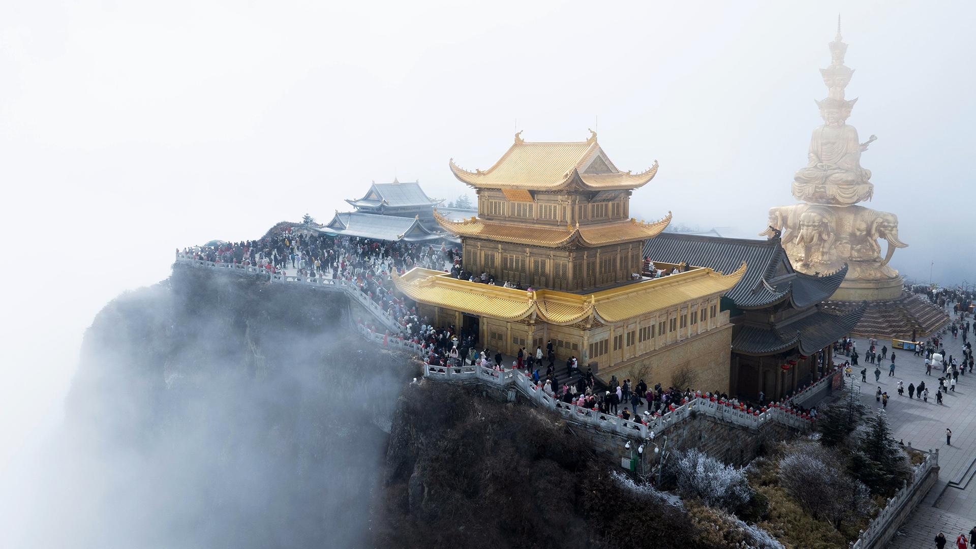 Zahlreiche Menschen besuchen einen goldenen Tempel auf dem Gipfel eines Berges im Nebel. | Jiang Hongjing/XinHua/dpa