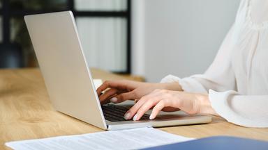 Hände einer Frau, die einen Laptop benutzt.