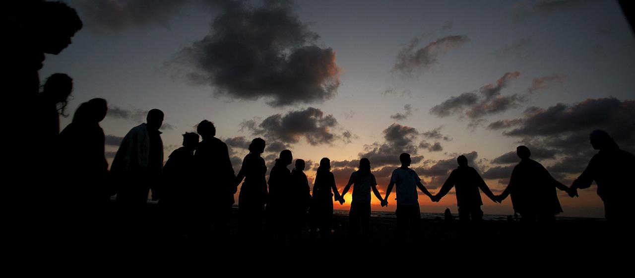 Menschen stehen bei Sonnenuntergang Hand in Hand nebeneinander.