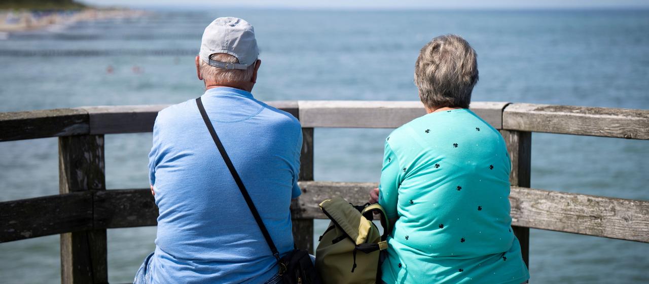 Zwei ältere Menschen blicken von der Seebrücke Graal-Müritz auf die Ostsee.
