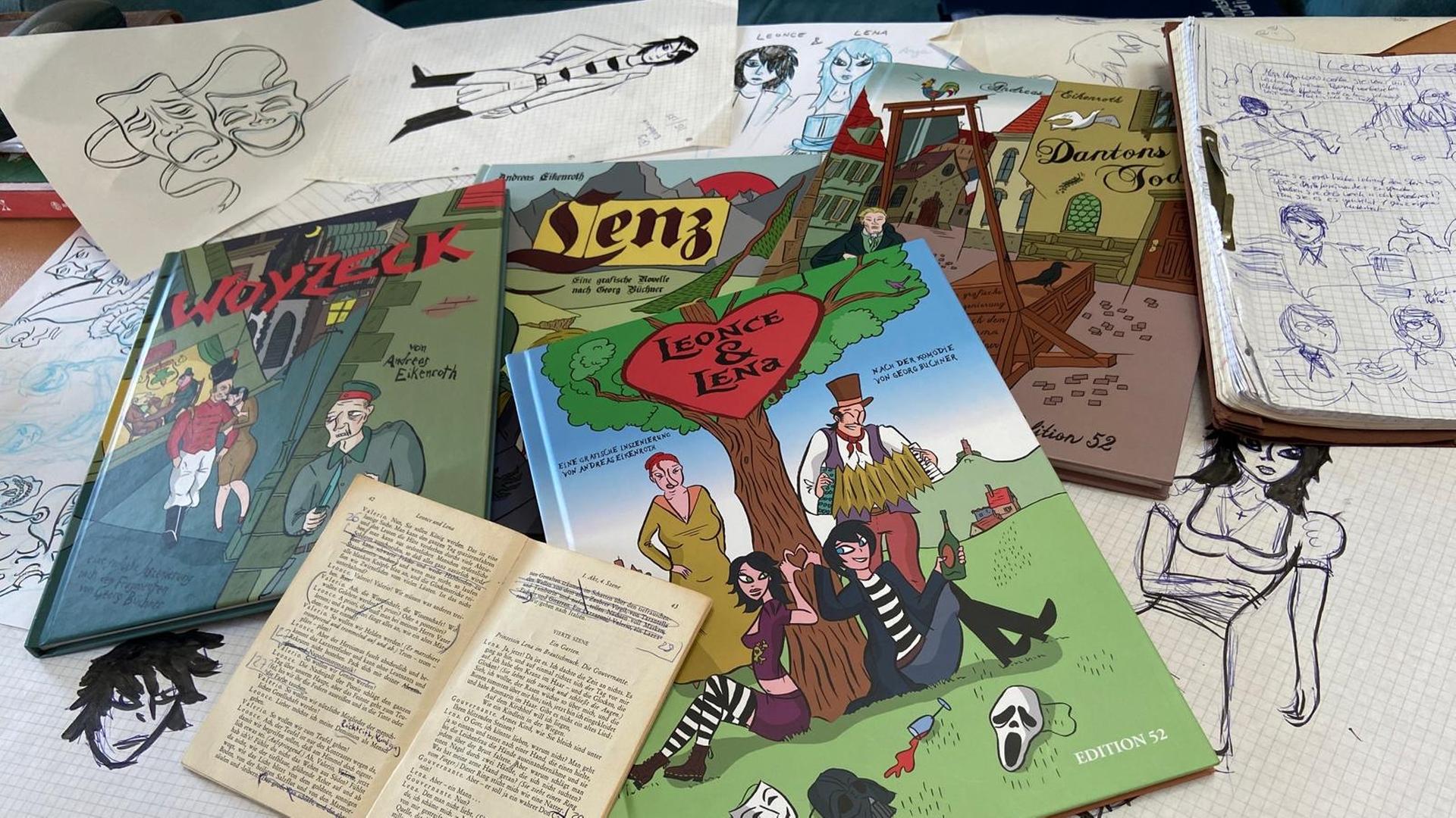 Auf einem Tisch liegen mehrere bunte Comicbücher sowie zahlreiche Skizzen und Zeichenentwürfe. | Alex Jakubowski (hr)
