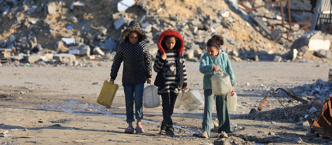 Drei Kinder holen Wasser zwischen Trümmern in Gaza-Stadt.