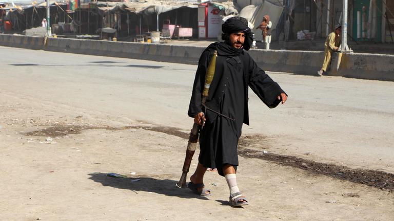 Ein Mann in schwarzer Kleidung läuft mit einem Gewehr in der Hand eine Straße entlang.