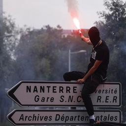 Demonstrant sitzt auf einem Wegweiser, auf dem Nanterre steht und hält einen Bengalisches Feuer.