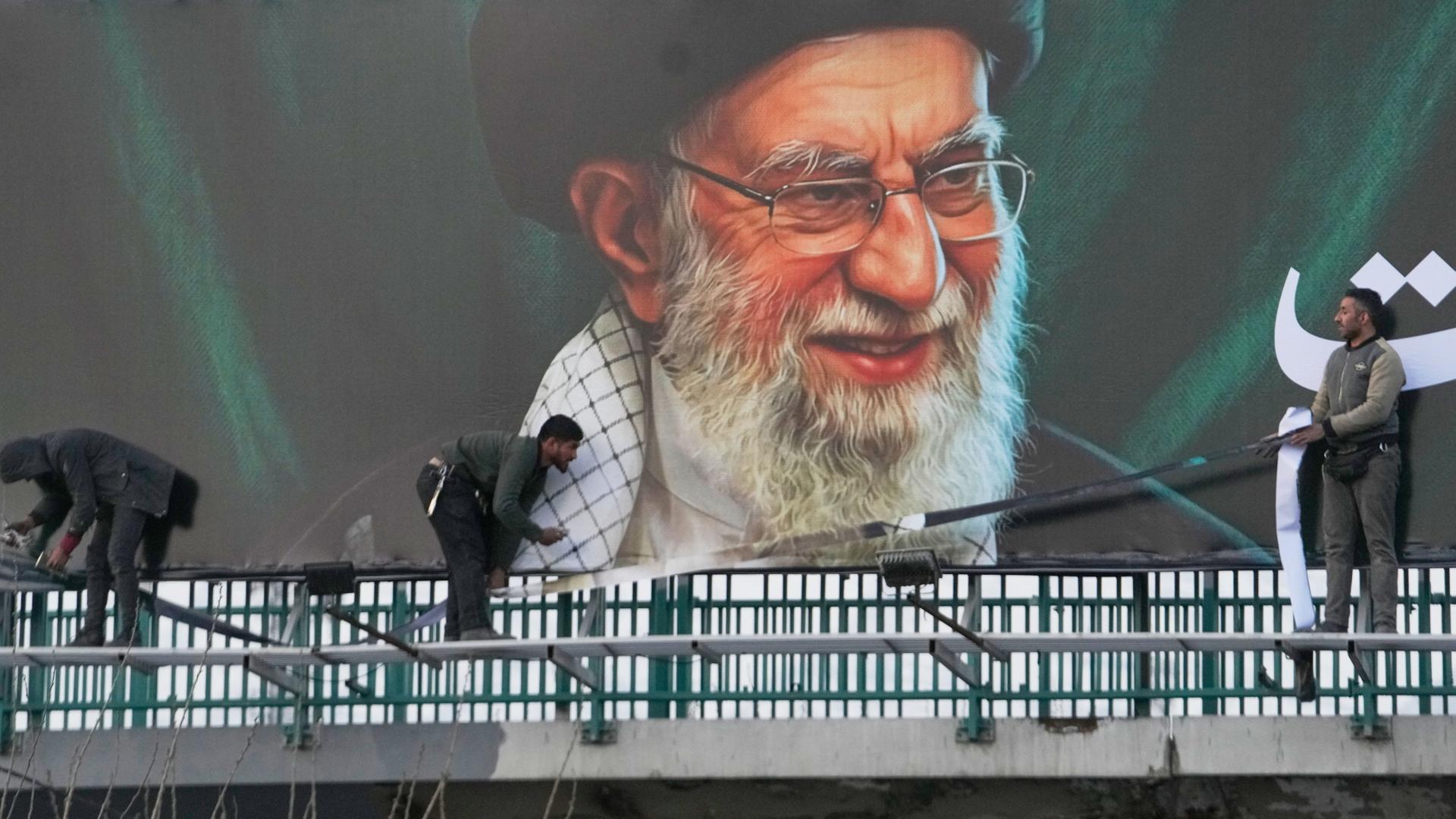 Arbeiter montieren eine Plakatwand mit dem Porträt des verstorbenen iranischen Obersten Führers Chamenei. | Vahid Salemi/AP/dpa