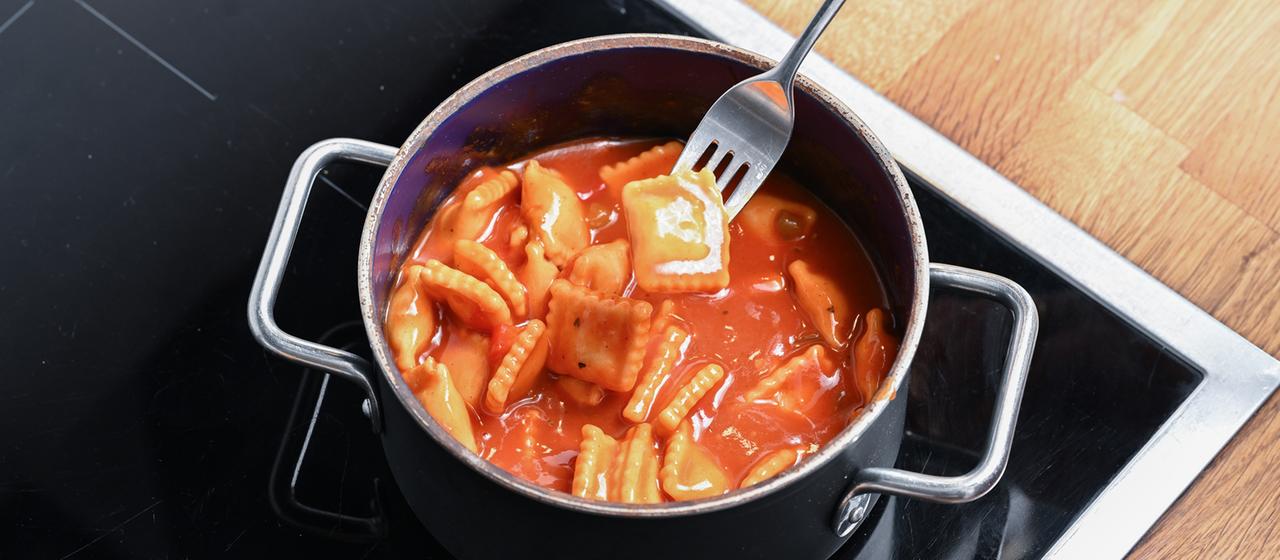Ein Topf mit Ravioli aus der Dose steht auf einem Herd. 