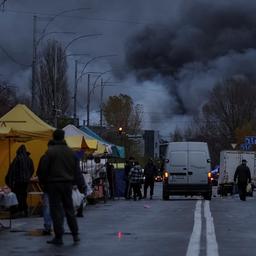 Menschen stehen auf einer Straße mit Marktständen, im Hintergrund steigt dichter schwarzer Rauch in den Himmel.