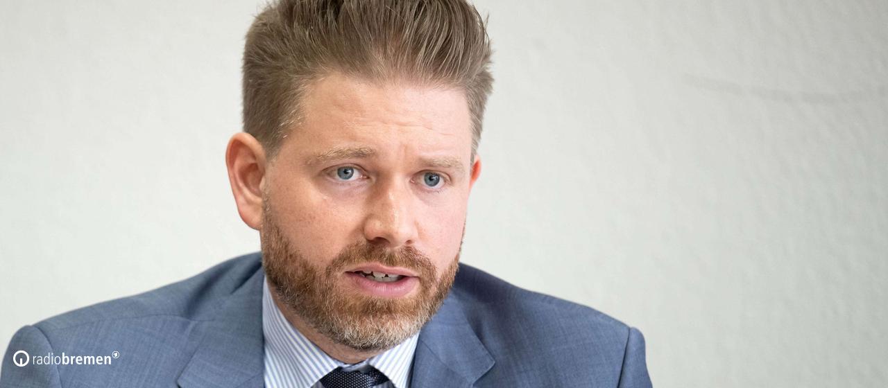 Thorge Koehler sitzt in Anzug an einem Tisch und spricht in einen butenunbinnen-Mikrofon