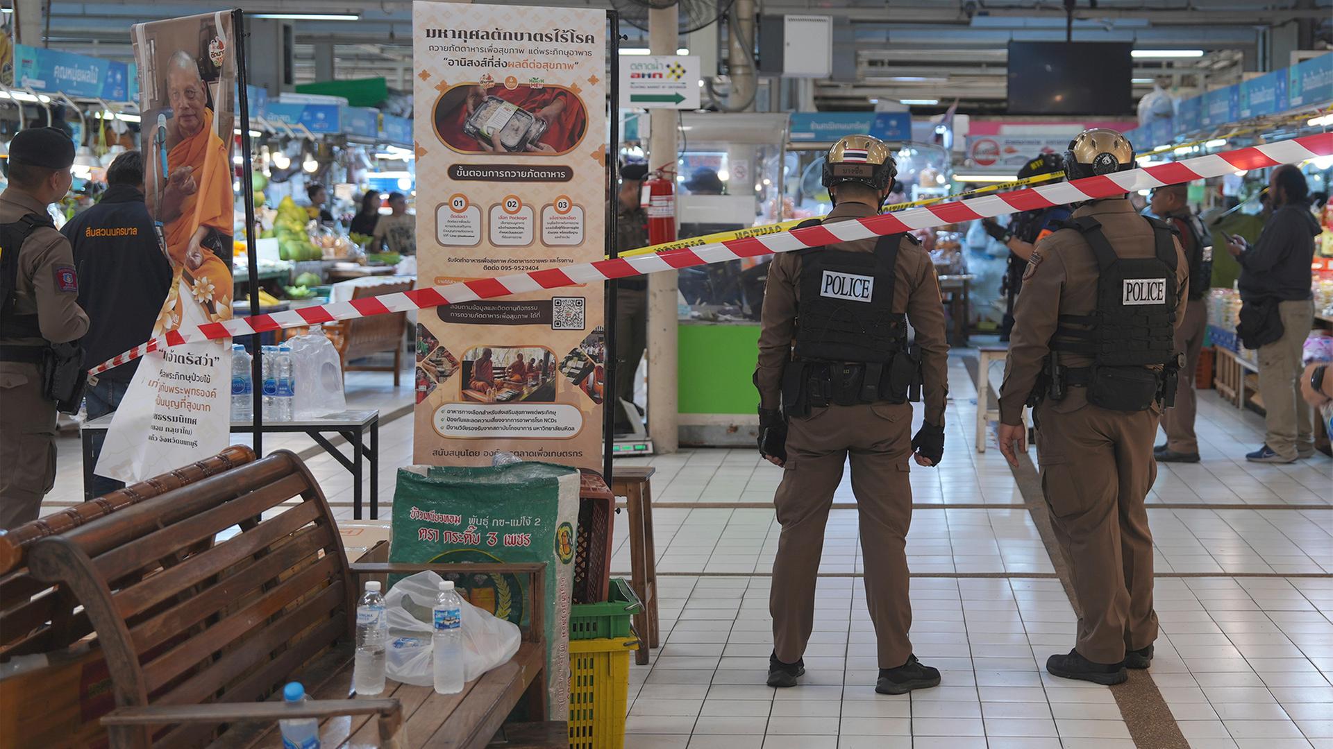 Polizisten stehen hinter einem Absperrband auf einem Markt in Bangkok. | dpa