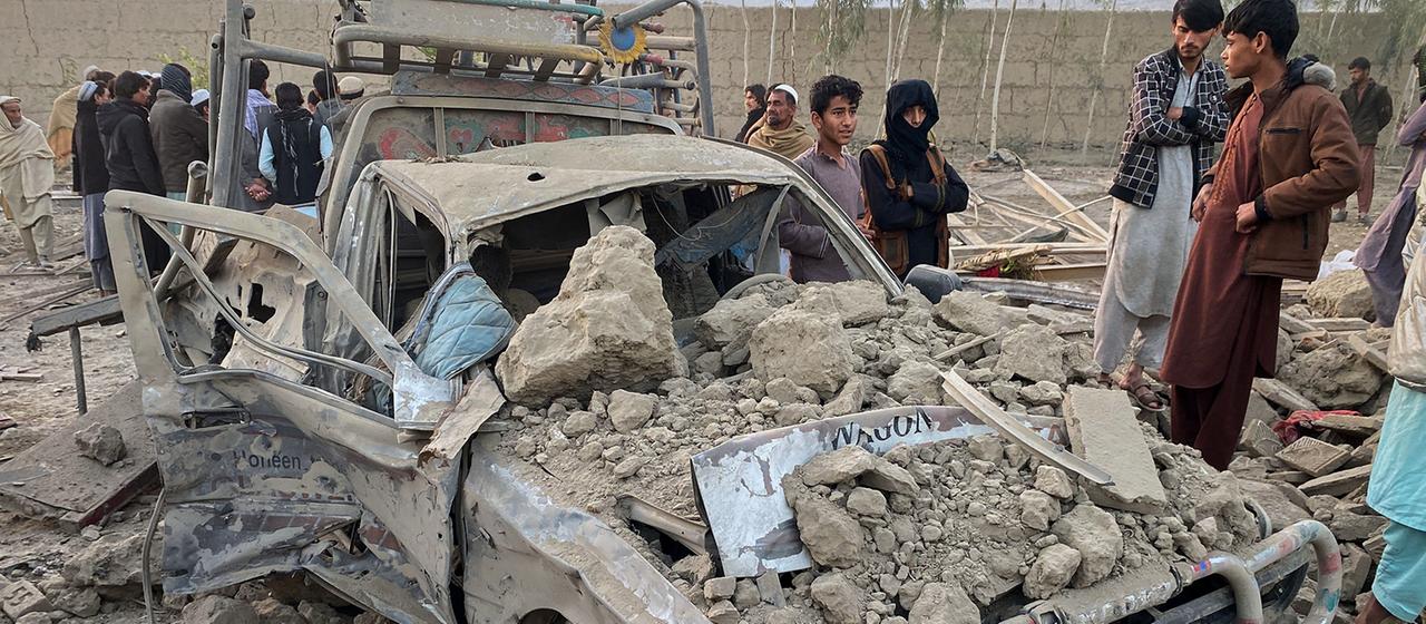 Menschen stehen neben einem von Trümmern überdeckten, zerstörten Fahrzeug.