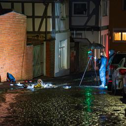 Dunkle Straße in kleinem Ort, auf Boden liegen undefinierbare Dinge auf einem Haufen, eine Polizistin macht Fotos