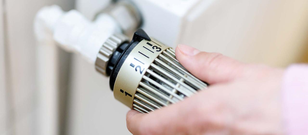 Eine Frau stellt an einem Thermostaten die Temperatur von einem Heizkörper ein.