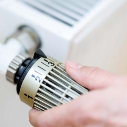 Eine Frau stellt an einem Thermostaten die Temperatur von einem Heizkörper ein.