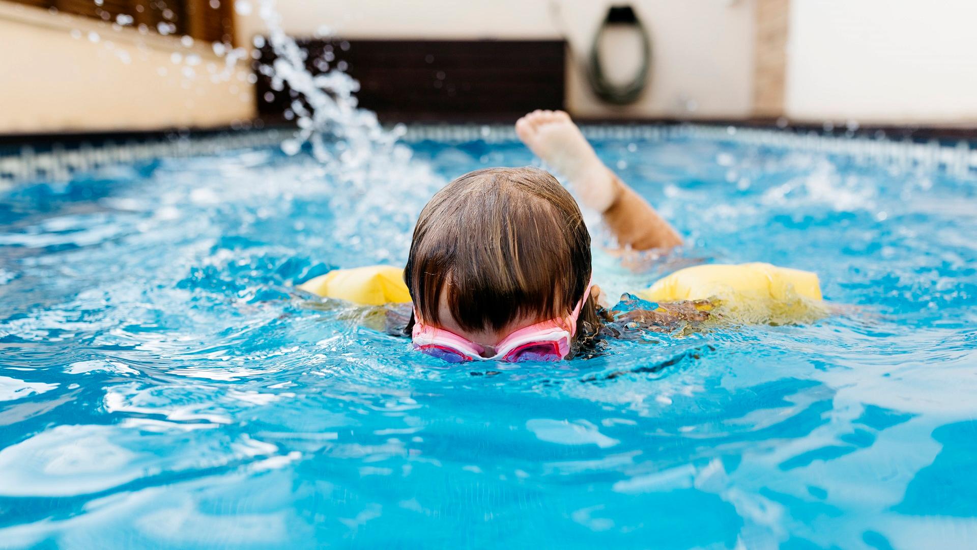 Ein Mädchen mit Schwimmbrille und Schwimmflügeln in einem Schwimmbecken | IMAGO / Westend61