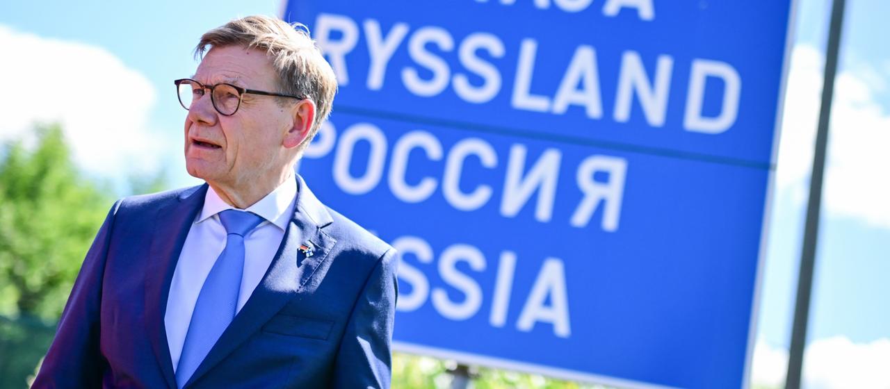 Johann Wadephul steht an der finnisch-russischen Grenze vor einem Schild, auf dem in mehreren Sprachen "Russland" geschrieben steht.