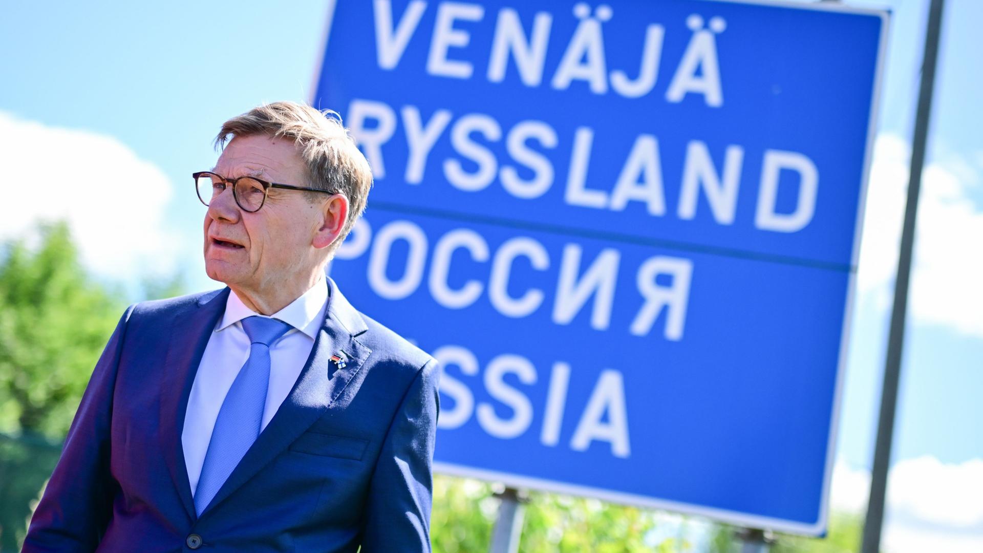 Johann Wadephul steht an der finnisch-russischen Grenze vor einem Schild, auf dem in mehreren Sprachen 