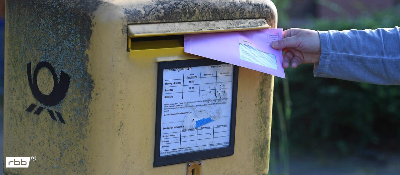 Symbolbild:Eine Person steckt einen Wahlbrief in einen Postkasten.(Quelle:picture alliance/Revierfoto)