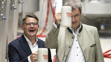Boris Rhein (li.) und Markus Söder halten bei der Besichtigung der Brauerei Glaabsbräu in Seligenstadt Bierkrüge in den Händen.