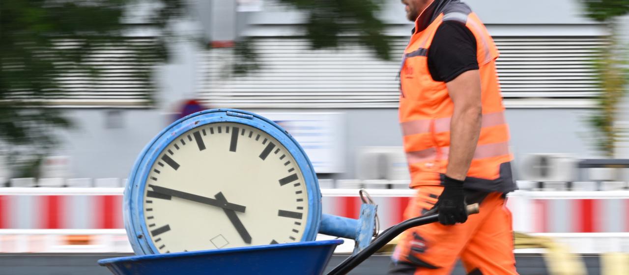 Ein Arbeiter transportiert eine Uhr auf einer Schubkarre