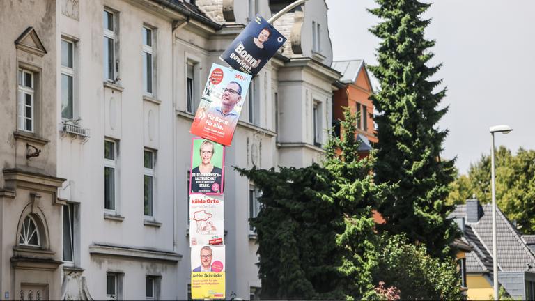 Wahlplakate verschiedener Kandidaten hängen an einem Laternenpfahl in Bonn. 