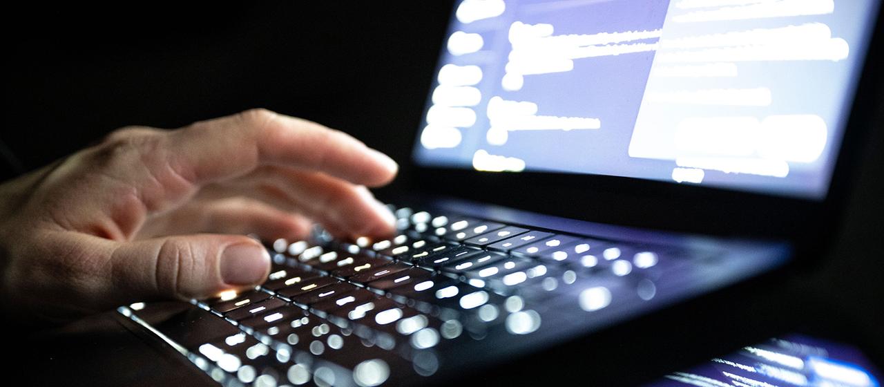 Eine Person tippt mit den Fingern auf einer beleuchteten Laptop-Tastatur.