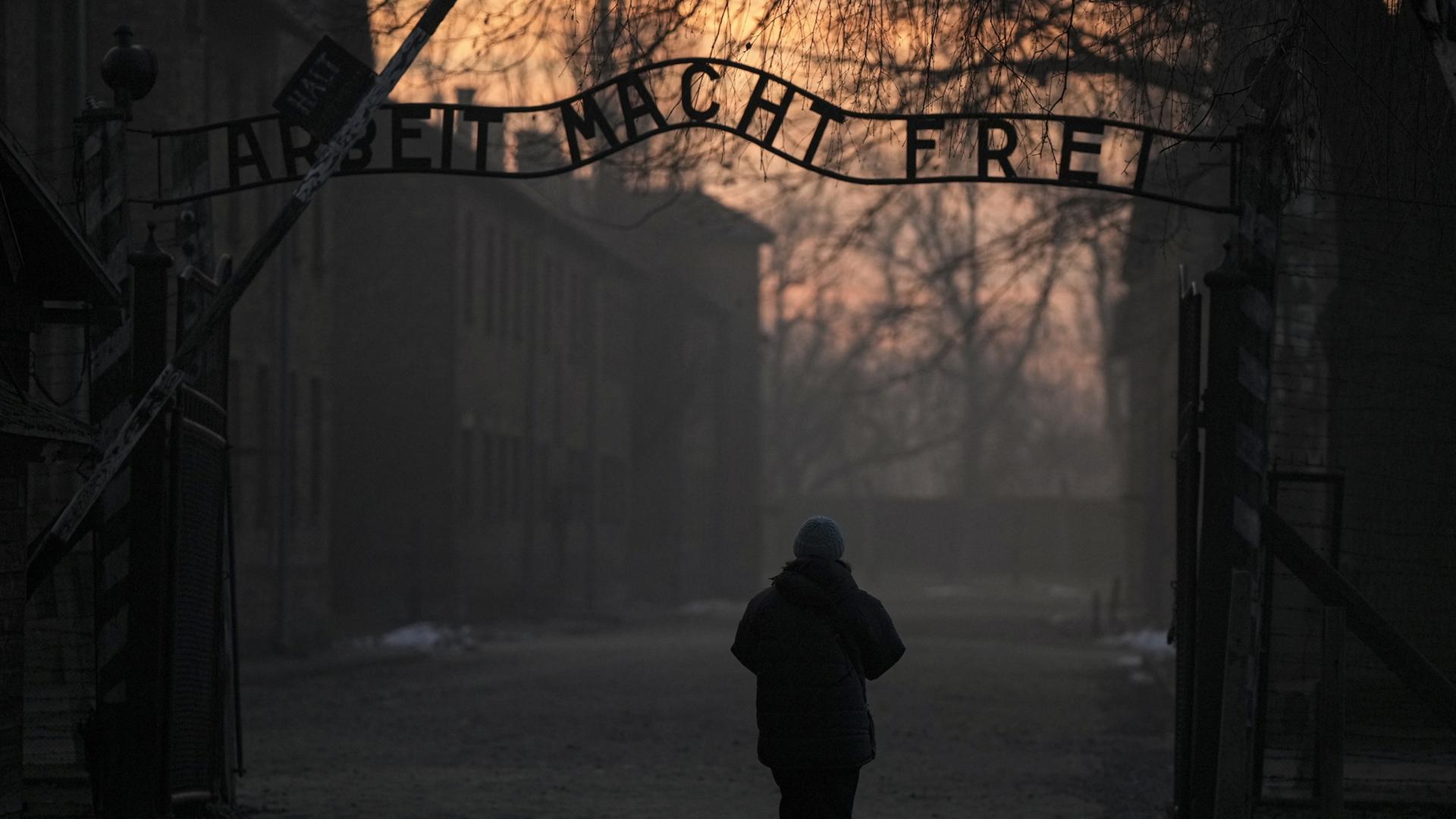 Eine Person geht zum Tor des ehemaligen deutschen Konzentrations- und Vernichtungslagers Auschwitz-Birkenau mit dem Schriftzug 