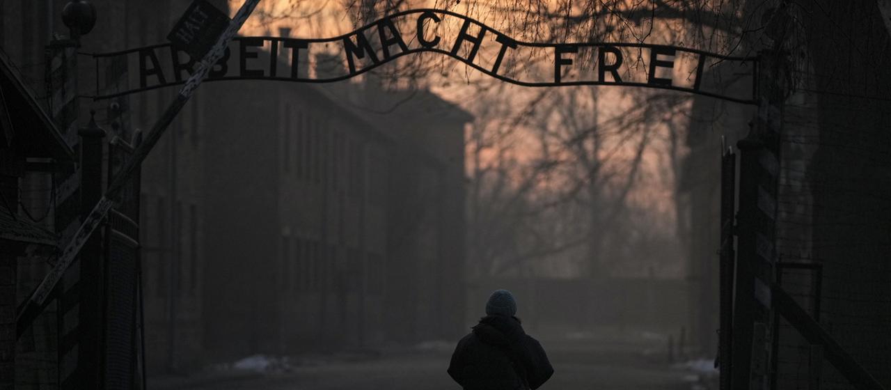 Eine Person geht zum Tor des ehemaligen deutschen Konzentrations- und Vernichtungslagers Auschwitz-Birkenau mit dem Schriftzug "Arbeit macht frei".
