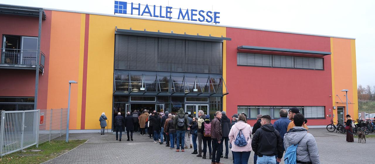 Wartende stehen vor einem Gebäude mit der Inschrift 