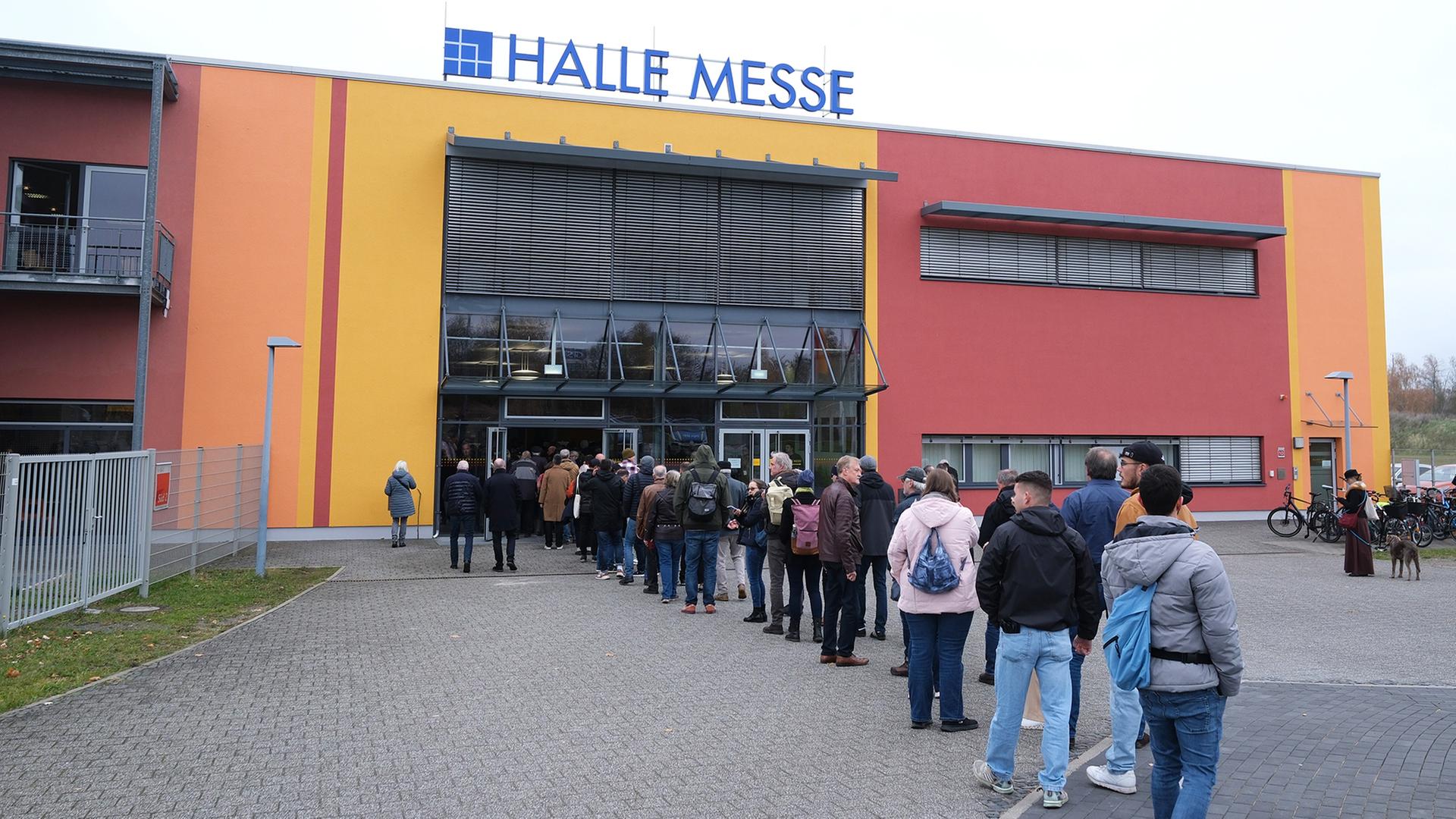 Wartende Menschen stehen vor einem Gebäude mit der Aufschrift 