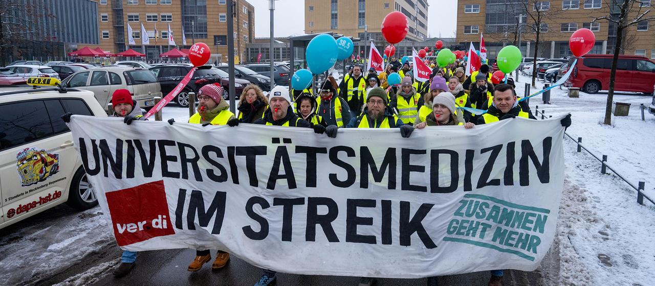 Teilnehmer einer Demonstration in Greifswald halten Ballons in die Luft und tragen ein Banner. 