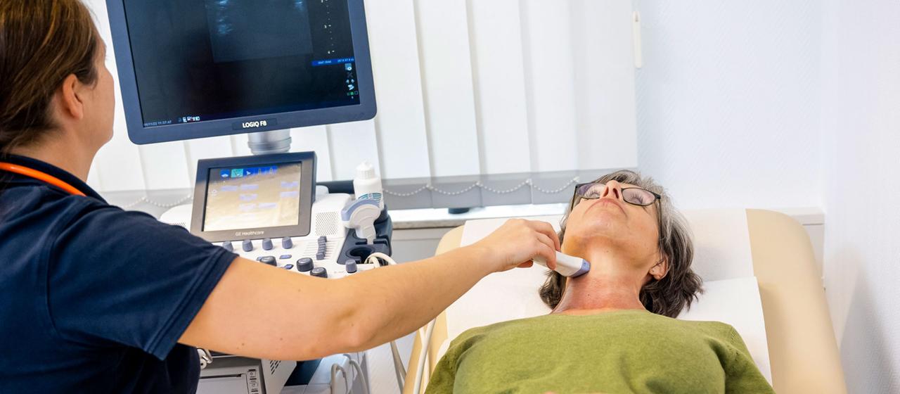 Eine Hausärztin führt eine Ultraschalluntersuchung der Schilddruese durch.