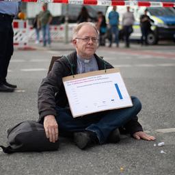 Jörg Alt sitzt protestierend auf der Straße und hat sich eine Hand am Asphalt festgeklebt.