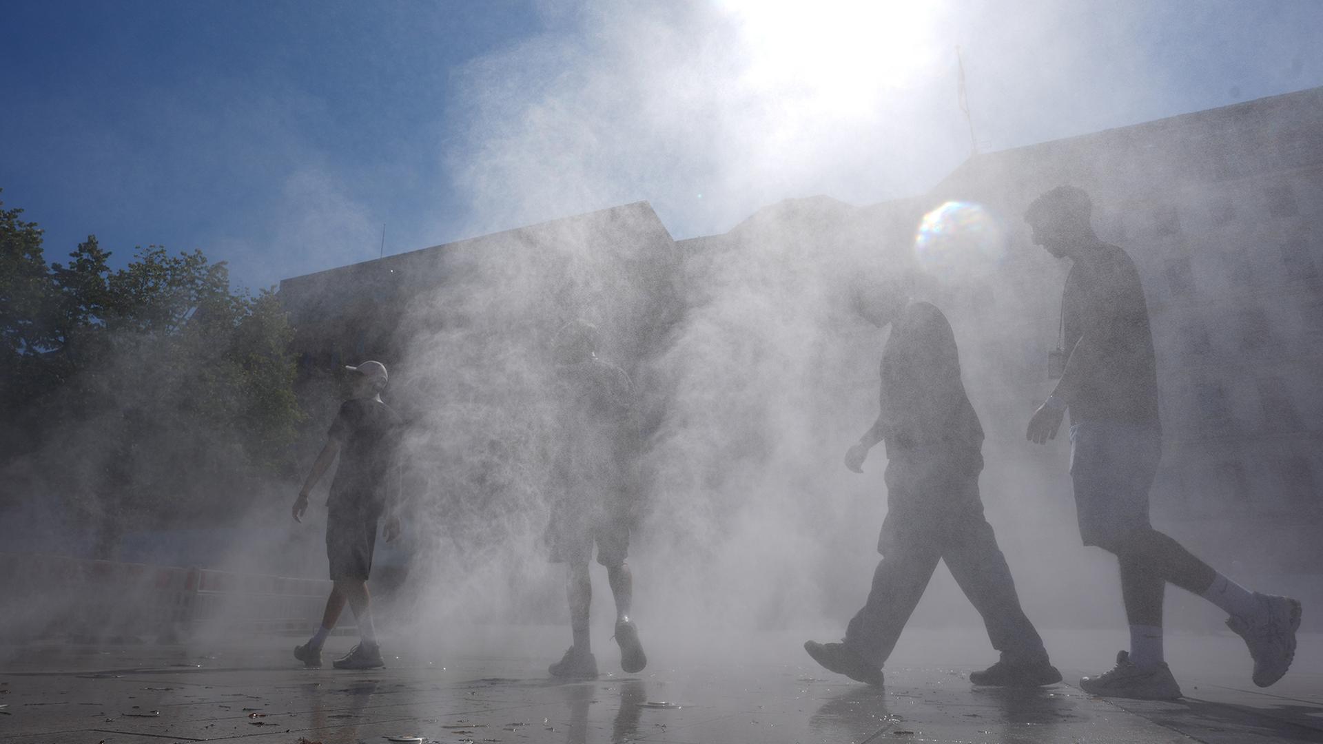 Passanten gehen in Hamburg durch einen Sprühnebel eines Wasserzerstäubers. | picture alliance/dpa