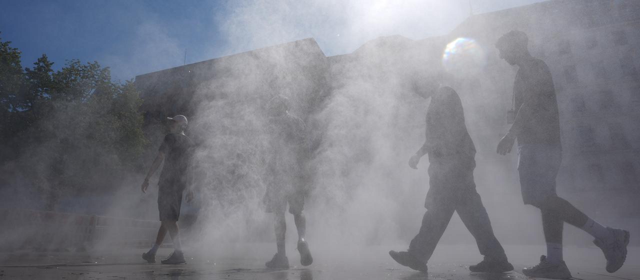 Passanten gehen in Hamburg durch einen Sprühnebel eines Wasserzerstäubers.