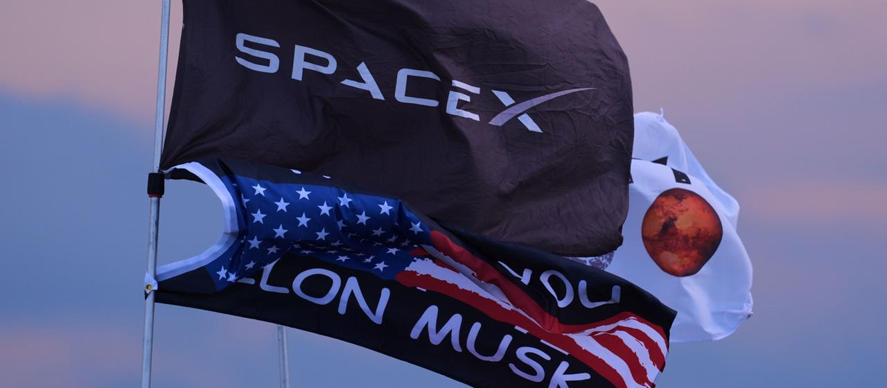 Mehrere Flaggen, darunter zwei mit dem Aufdruck SpaceX und Elon Musk, sind  in der Nähe des Geländes in Texas aufgestellt