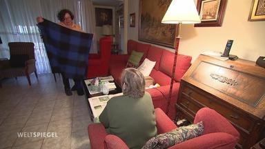Eine Frau legt in einem Wohnzimmer eines älteren Mannes eine Decke zusammen