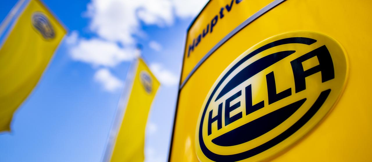 Logo des Autozulieferers Hella ist auf einem Schild neben Fahnen zu sehen