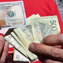 Ein Mann hält einen 100-Dollar-Schein in der rechten Hand und in der linken argentinische Pesos-Banknoten.