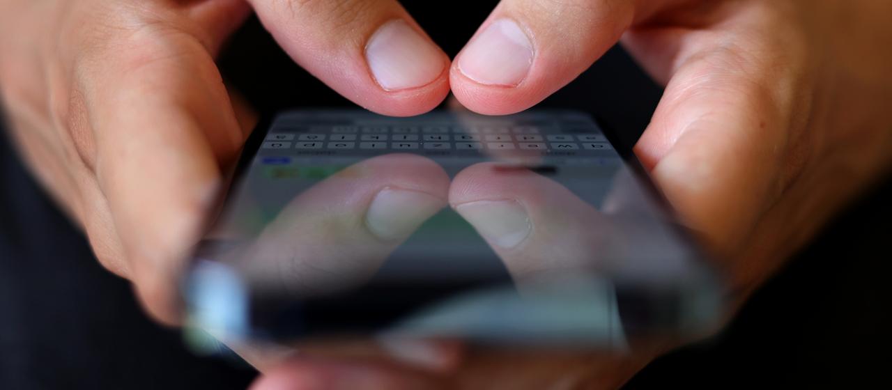 Ein Jugendlicher tippt auf einem Smartphone eine Nachricht.