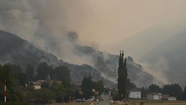Rauchwolken steigen hinter einem Ort von Hängen auf.