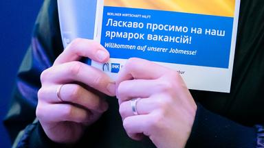 Eine Frau hält bei einer Jobmesse für ukrainische Geflüchtete von der IHK Berlin und der Agentur für Arbeit den Messeplan mit der ukrainischen Flagge.